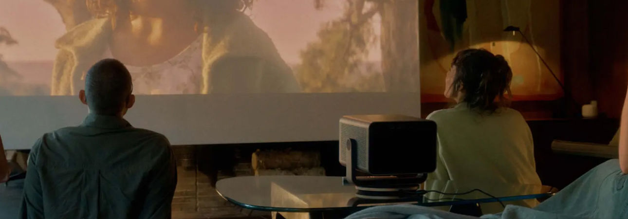 Lifestyle image of a couple watching a movie on a large screen in a cosy, dimly lit living room with the Leica Cine Play 1 projector